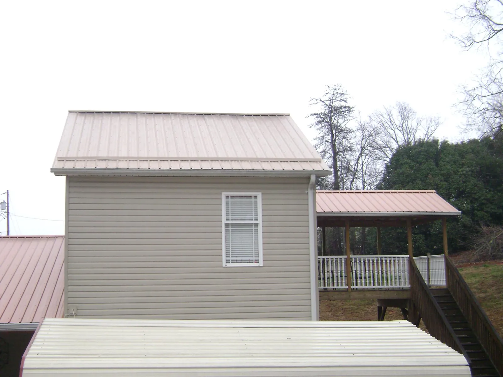 Tan metal roofs on a two story addition and attached porch, from a Roof Replacement job in Santa Fe